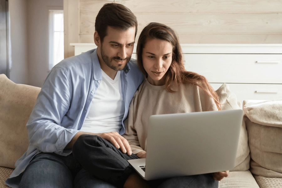 couple sitting on the couch looking at the computer together 